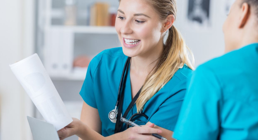 Eine junge Frau im grünen Kasack lächelt und schaut dabei auf Patientenunterlagen.