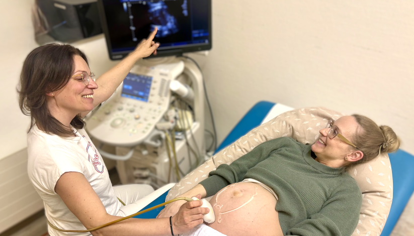 Eine Ärzte macht einen Ultraschall bei einer schwangeren Frau. Beide lächeln.