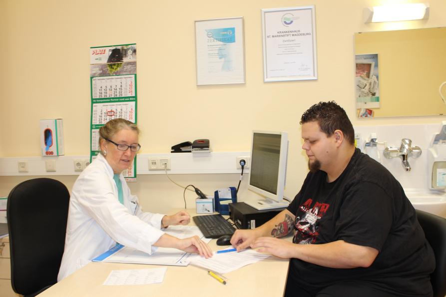 Frau Professor Wolff im Gespräch mit Adipositaspatient Lukas Schneider. Beide sitzen Schreibtisch.