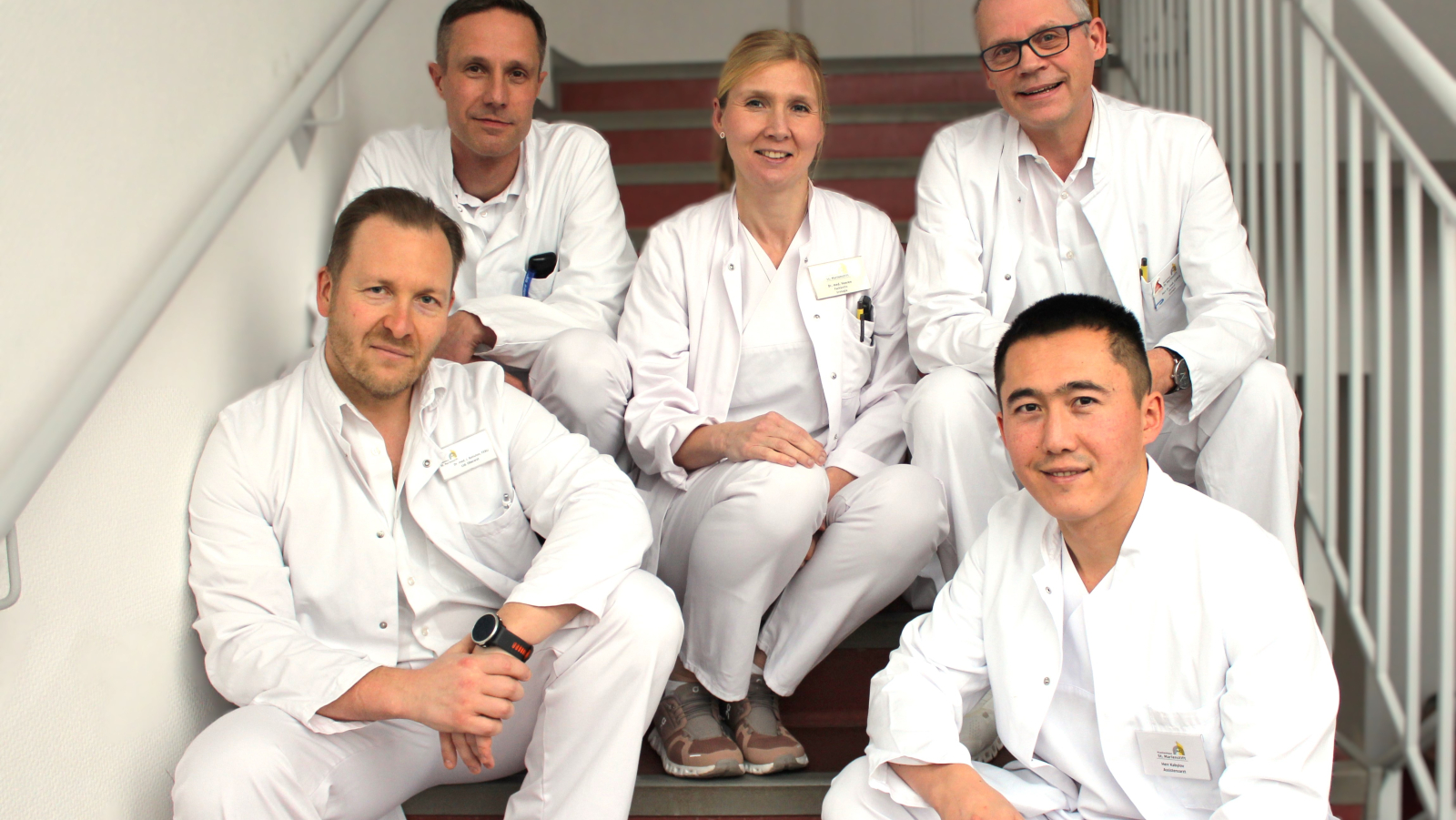 Die Ärzte der Klinik für Urologie sitzen auf einer Treppe und schauen lächelnd und zugewandt in die Kamera.