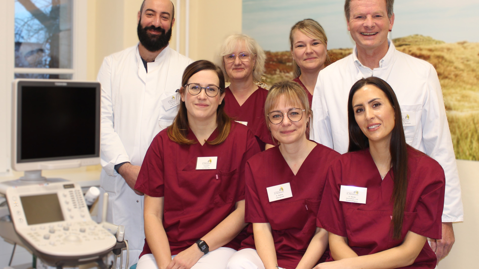 Das Team des Brustzentrums, vier Damen in weinroten Kasaks und links und rechts zwei Herren in weißen Arztkitteln lächeln in die Kamera.