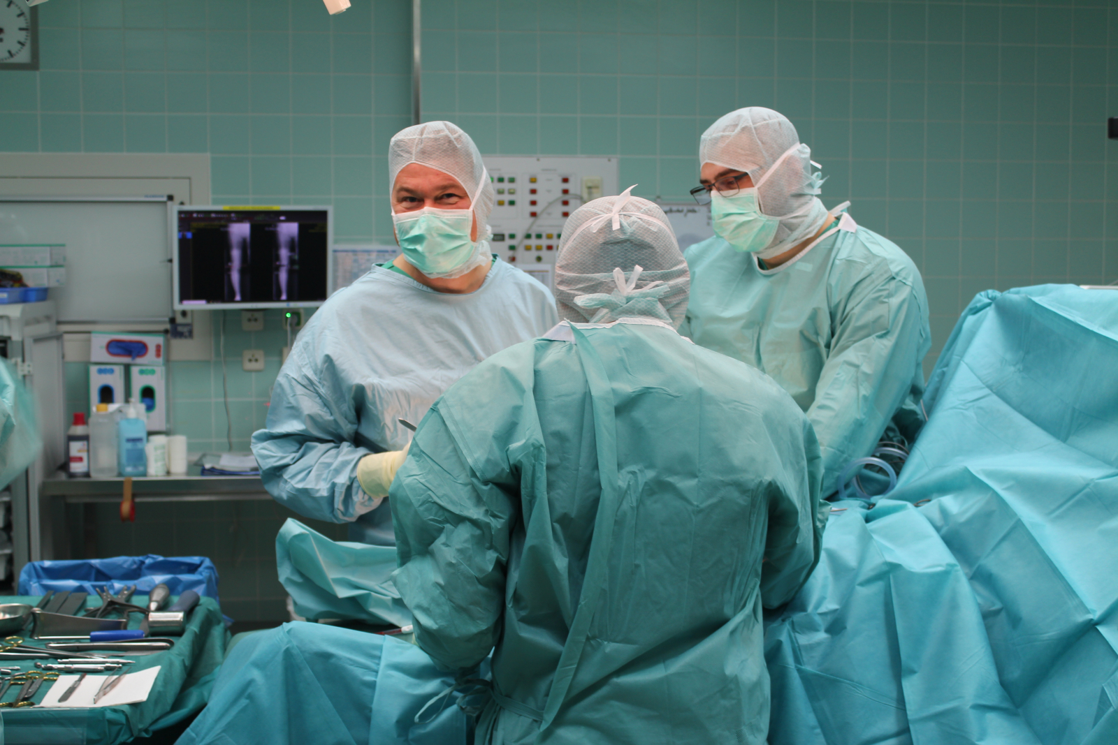 Drei Operateure stehen während einer OP am Operationstisch. Ein Operateur lächelt in die Kamera.