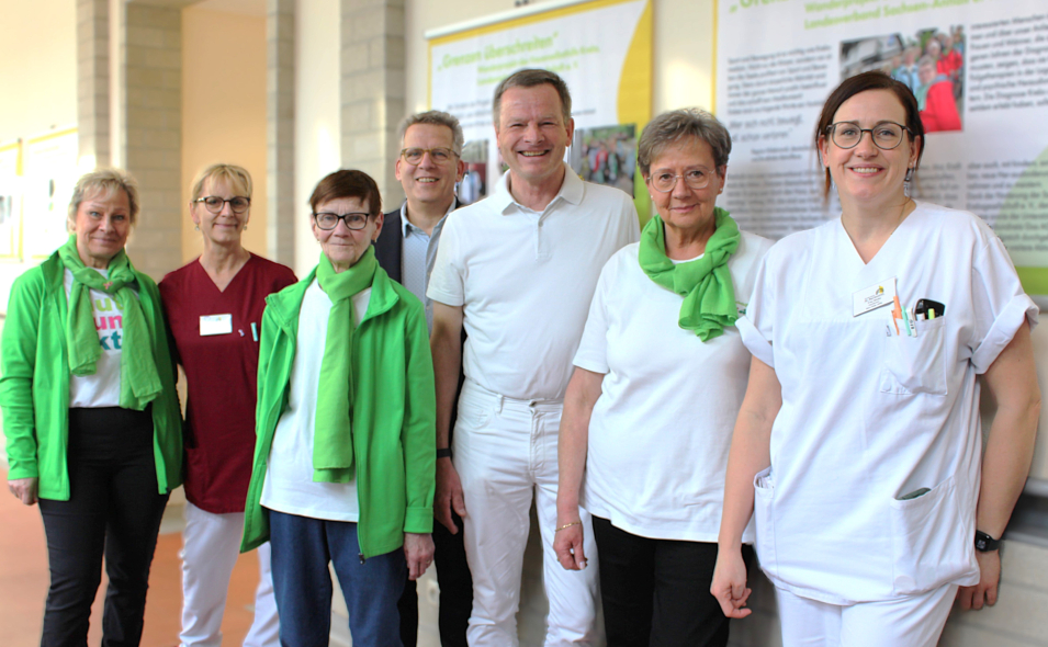 Von links nach rechts: Kerstin Seitz (Frauenselbsthilfegruppe Krebs), Katrin Hahn (Stationsverantwortliche im Brustzentrum) Hannelore Pofahl (Selbsthilfegruppe Krebs), Johannes Brumm (Geschäftsführer St. Marienstift), Dr. Wolfgang Hartmann (Chefarzt der Frauenheilkunde und Geburtshilfe), Rita Schneider (Leiterin der Frauenselbsthilfegruppe Krebs in Sachsen-Anhalt) Kristin Nüske, Fachärztin für Frauenheilkunde im Brustzentrum am St. Marienstift). Alle stehen vor einem Exponat der Ausstellung und lächeln.