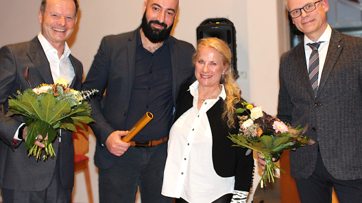 Von links nach rechts erkennen Sie Dr.  Wolfgang Hartmann, Chefarzt der Frauenheilkunde & Geburtshilfe mit einem Blumenstrauß, Khaled Benfoughal, neuer Leiter des Brustzentrums mit dem Staffelstab, Dr. Kristina Freese, die scheidende Leiterin des Brustzentrums, Dr. med. Michael Ludwig, Ärztlicher Direktor.